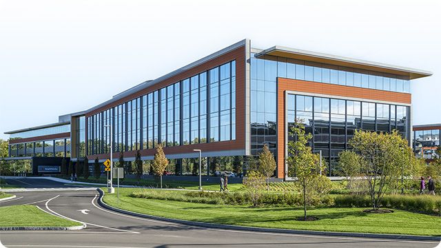 Edificio con grandes ventanales y diseño contemporáneo rodeado de vegetación, con una calzada con curvas en primer plano.