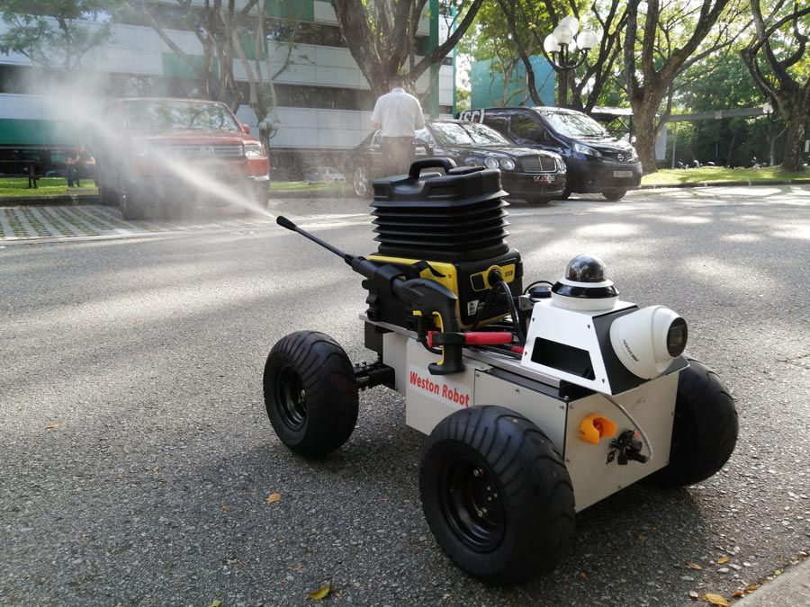 The Weston Robot protype on a paved street, actively spraying outside. Cars and a person in the background of the image.